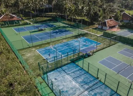 Aerial view of the open-air blue padel court with a shade canopy beside it, set among the resort's tennis courts and palm trees
