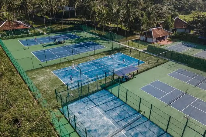 Aerial view of the open-air blue padel court with a shade canopy beside it, set among the resort's tennis courts and palm trees