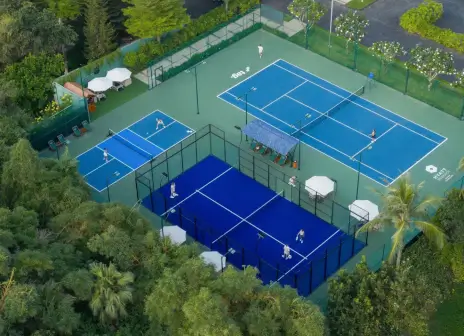 Aerial view of the open-air blue padel court between a tennis court and two pickleball courts, with loungers and parasols alongside