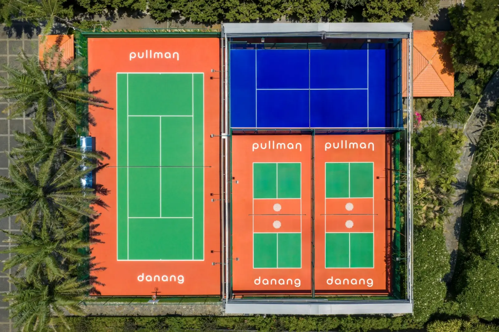 Aerial view of the blue padel court under its retractable roof, beside a tennis court and two pickleball courts