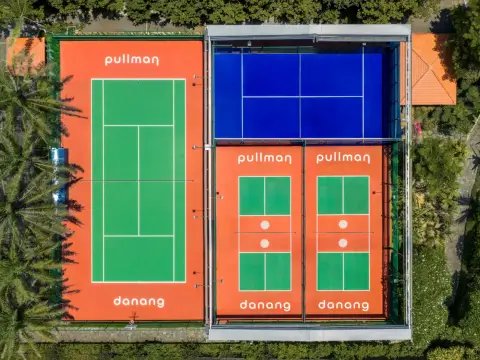 Aerial view of the blue padel court under its retractable roof, beside a tennis court and two pickleball courts